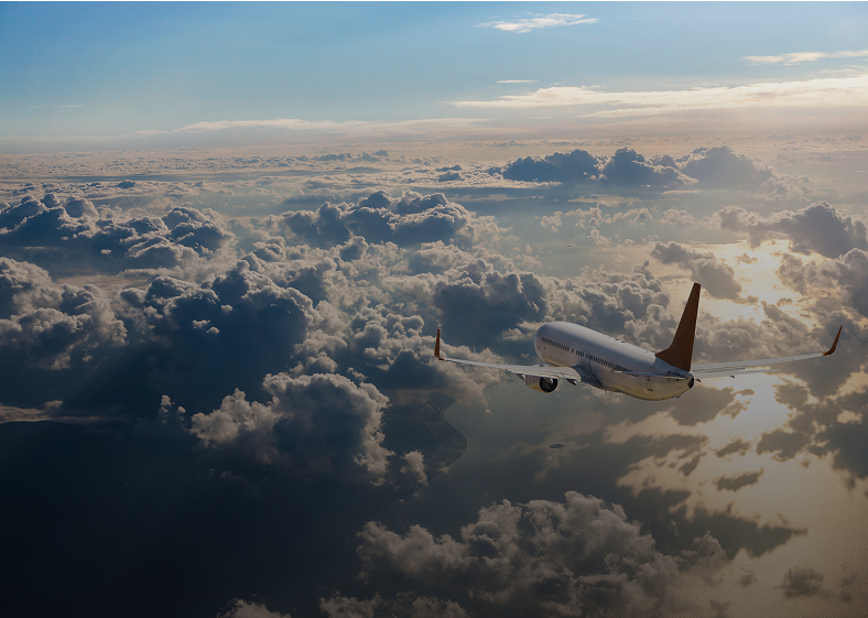 Airplane flying above clouds during sunset.