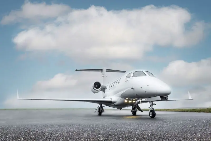A small private jet parked on the runway under a cloudy sky.
