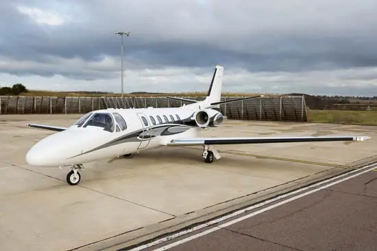 Private jet parked on tarmac under cloudy sky.