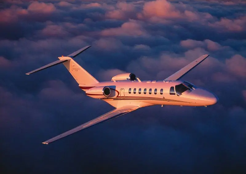 A private jet flying above clouds at sunset.