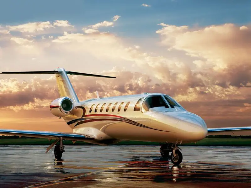 A sleek private jet on a wet runway during sunset.