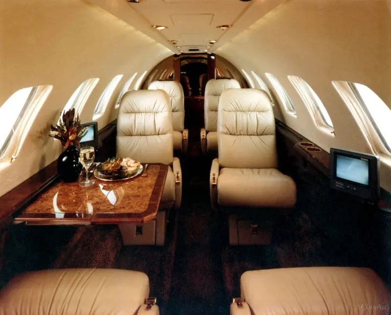 Luxurious private jet interior with plush beige leather seats and wooden table.