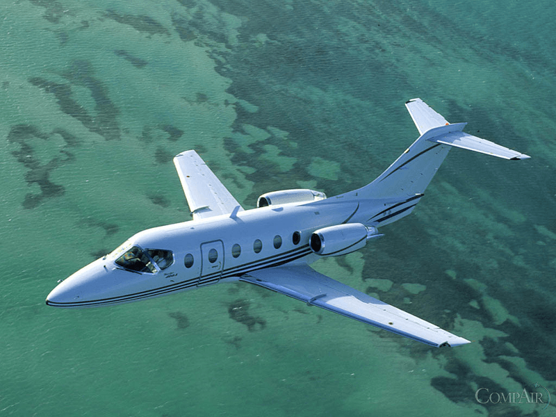 A white private jet flying over clear turquoise waters.