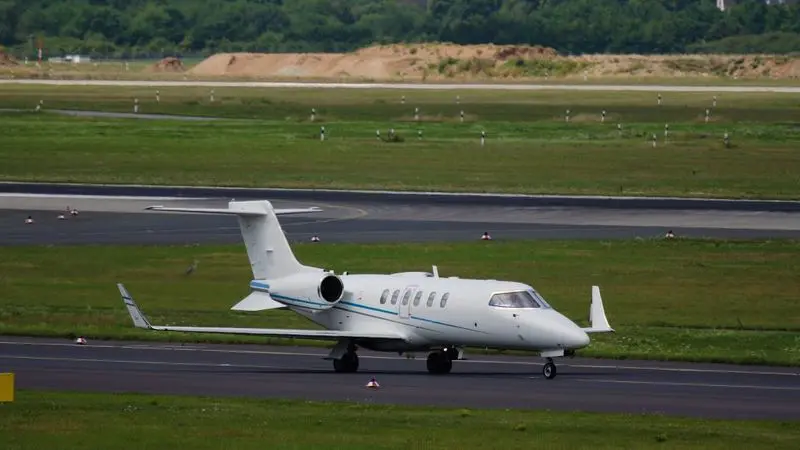 Private jet taxiing on runway with green hills in background.