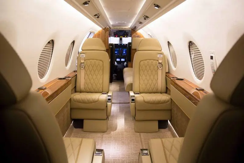 Luxurious private jet interior with beige leather seats and wood accents.