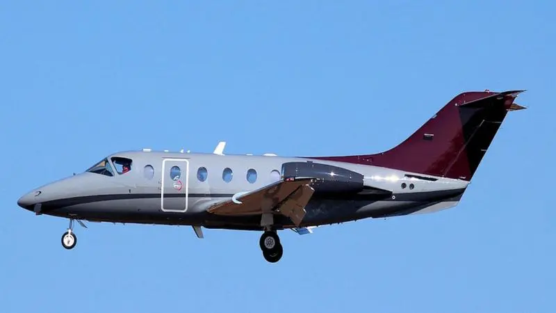 A small private jet flying against a clear blue sky.