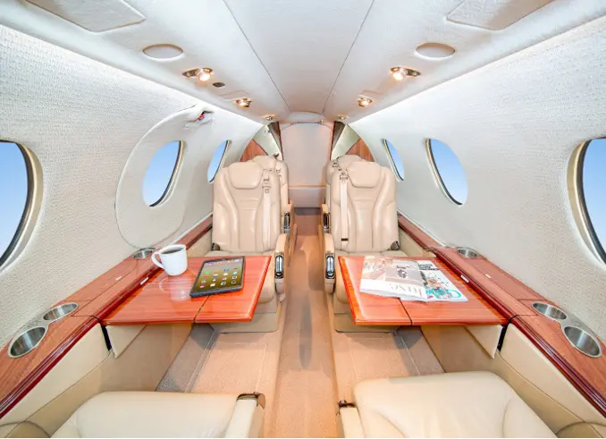 Luxurious private jet interior with beige leather seats and wooden tables.