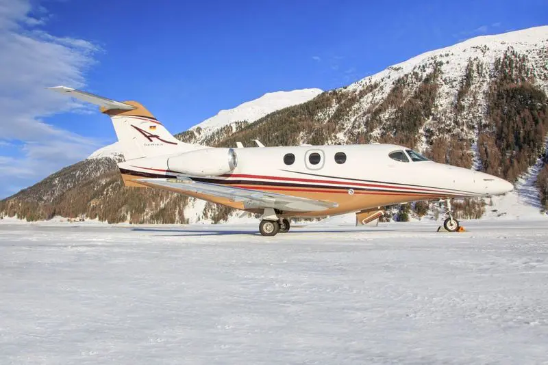 Private jet parked on snowy runway with mountains in background.