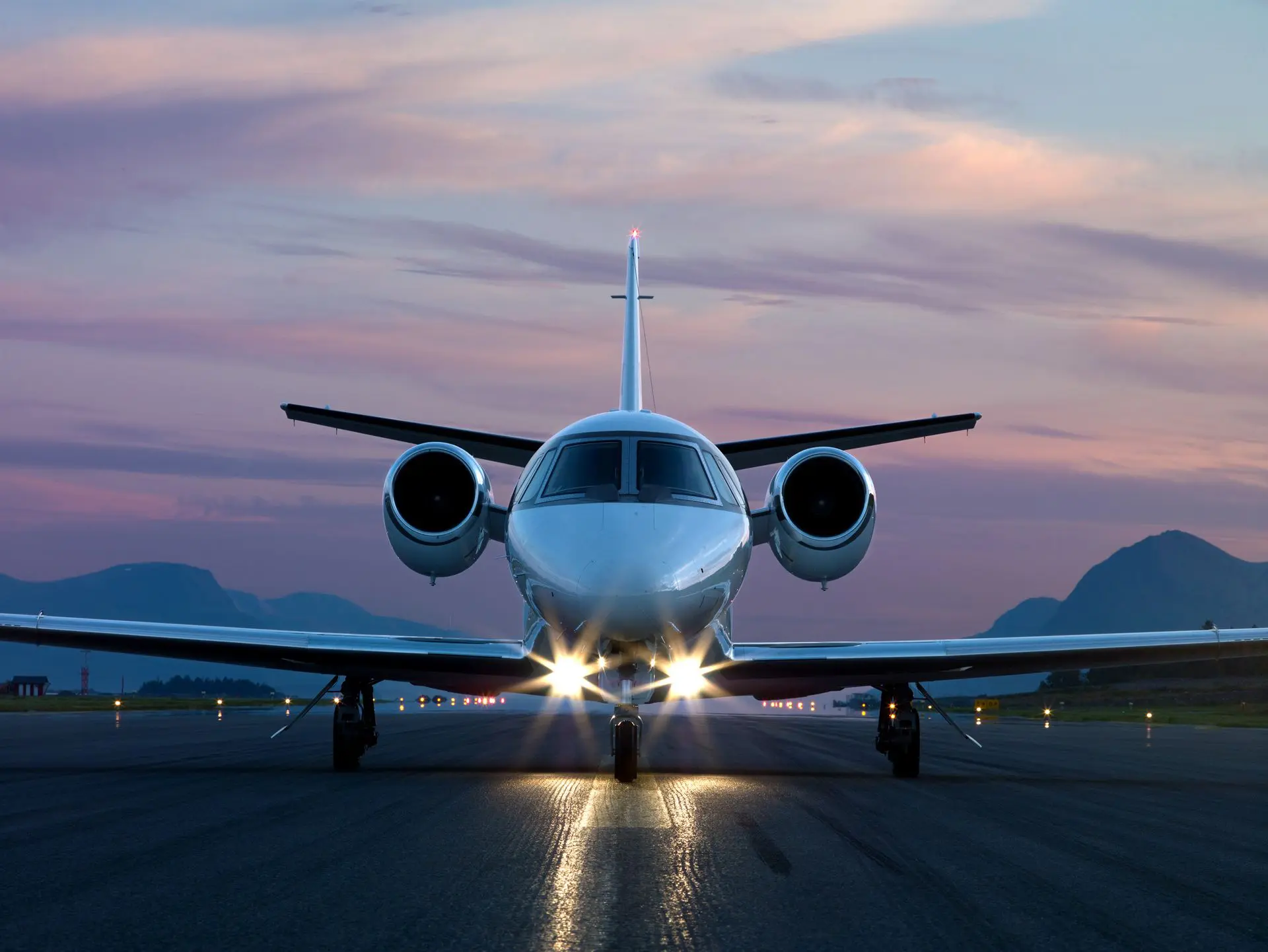 Private jet with lights on, ready for takeoff at dusk.