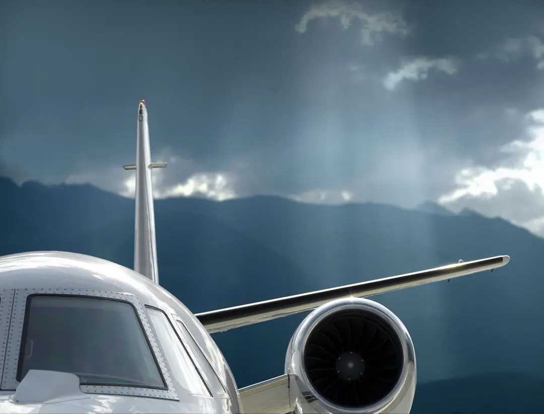 Close-up of airplane engine and tail with mountains in the background.