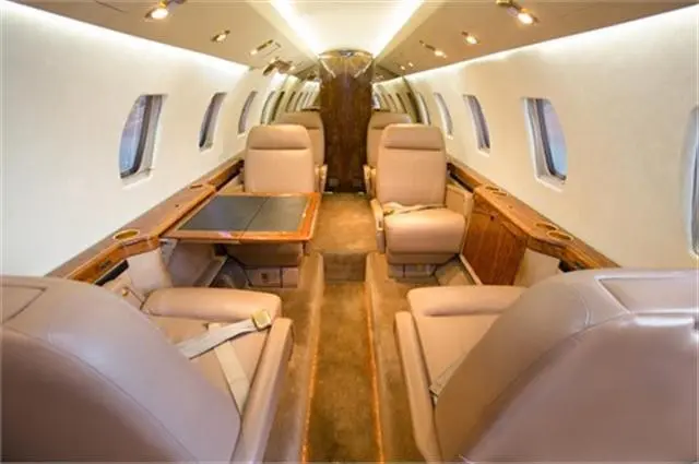 Luxurious private jet interior with beige leather seats and wooden accents.