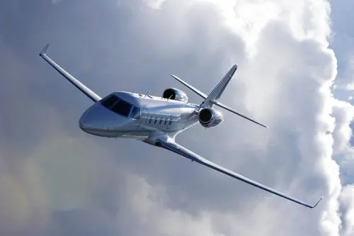 A sleek private jet flying through cloudy skies.
