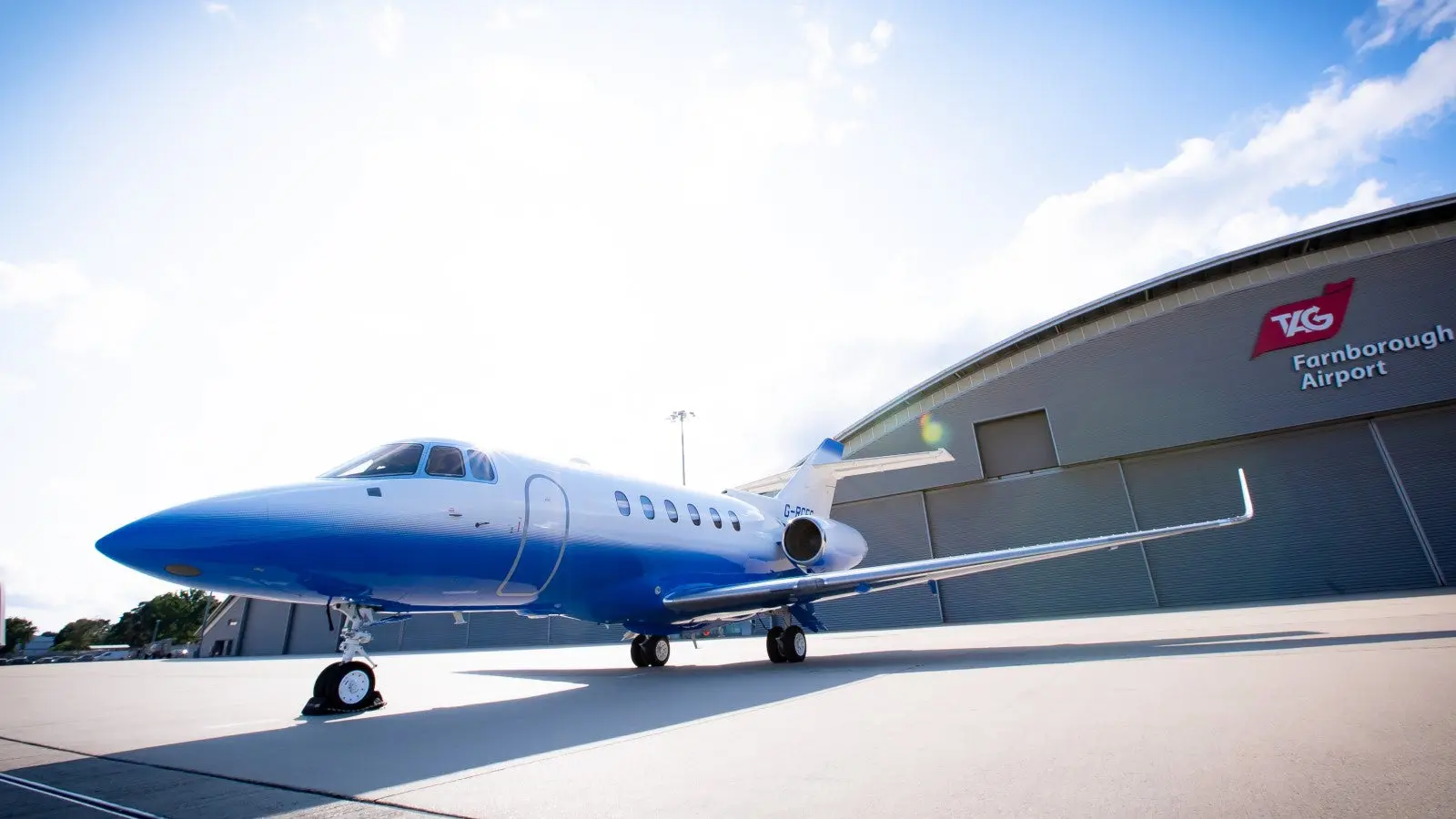 A sleek blue private jet parked on the runway on a bright day.