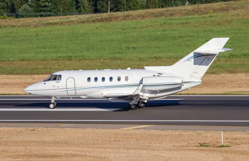 Private jet taxiing on runway with green field background.