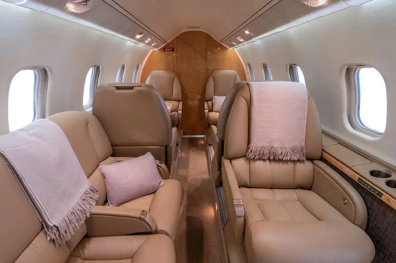 Luxurious private jet interior with beige leather seats and soft pink accents.