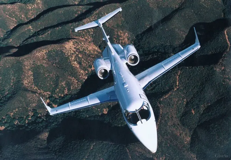 A sleek private jet flying over rugged terrain.