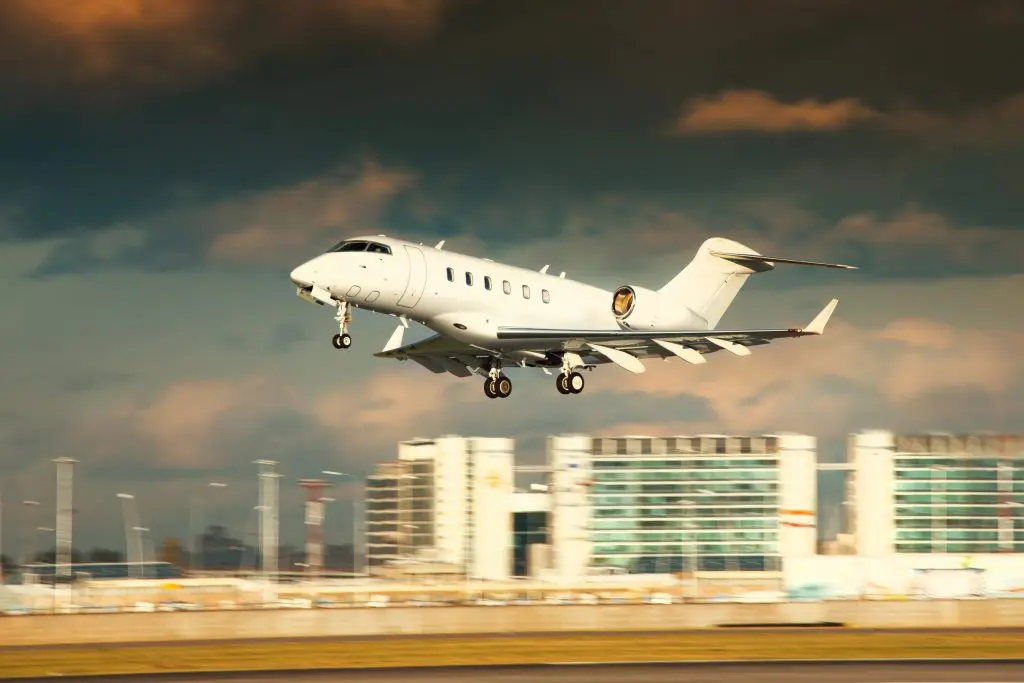 A private jet taking off during sunset with buildings in the background.
