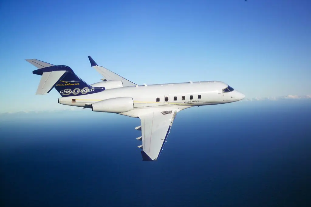 A private jet flying high over the ocean under a clear blue sky.