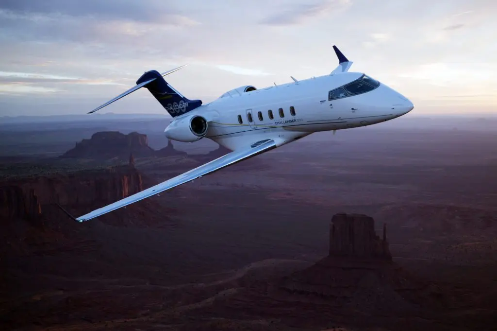 A private jet flying over a desert landscape at dusk.