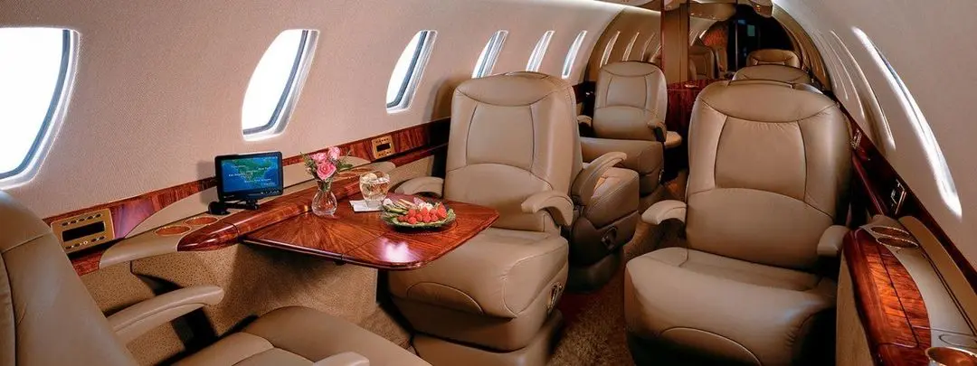 Luxurious leather seats inside a private jet with a wooden table and refreshments.