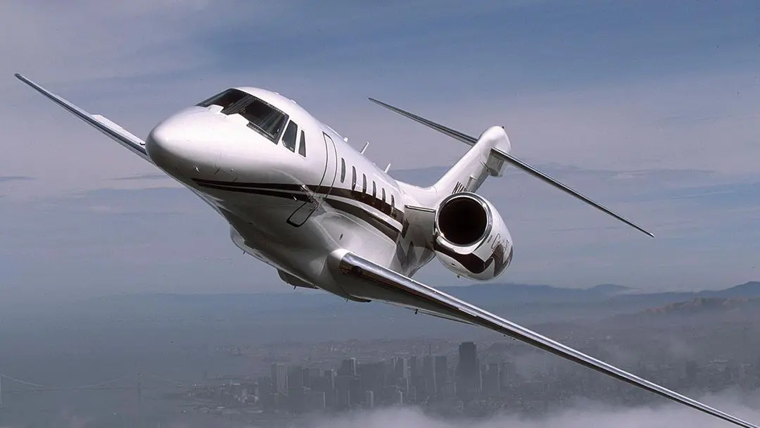 Private jet flying above a cityscape on a clear day.