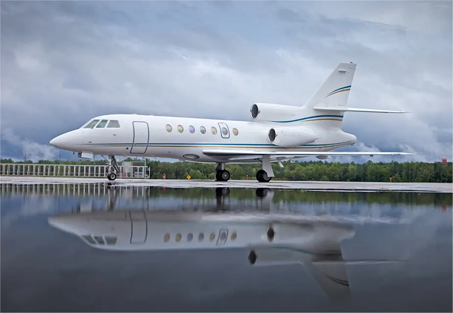 Private jet reflecting on wet tarmac under cloudy sky.