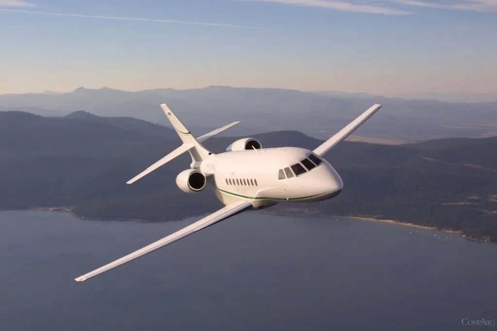 A sleek white private jet flying over mountains at sunset.