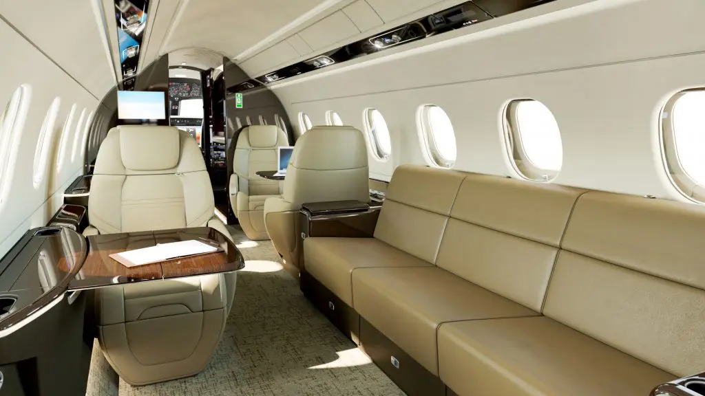 Luxurious interior of a private jet with beige leather seats and wood accents.