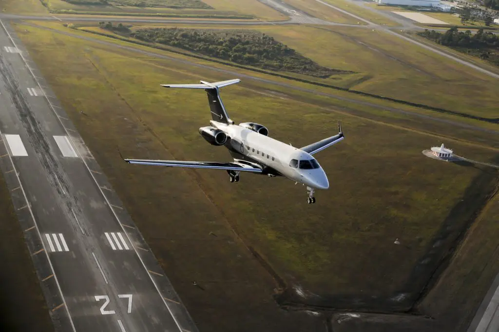 Private jet taking off from runway with scenic fields below.
