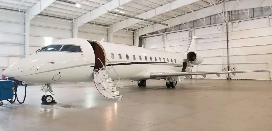 Private jet parked inside a spacious hangar with open door.