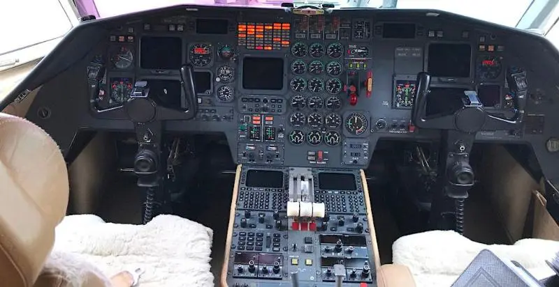 Cockpit view of an aircraft with numerous controls and screens.