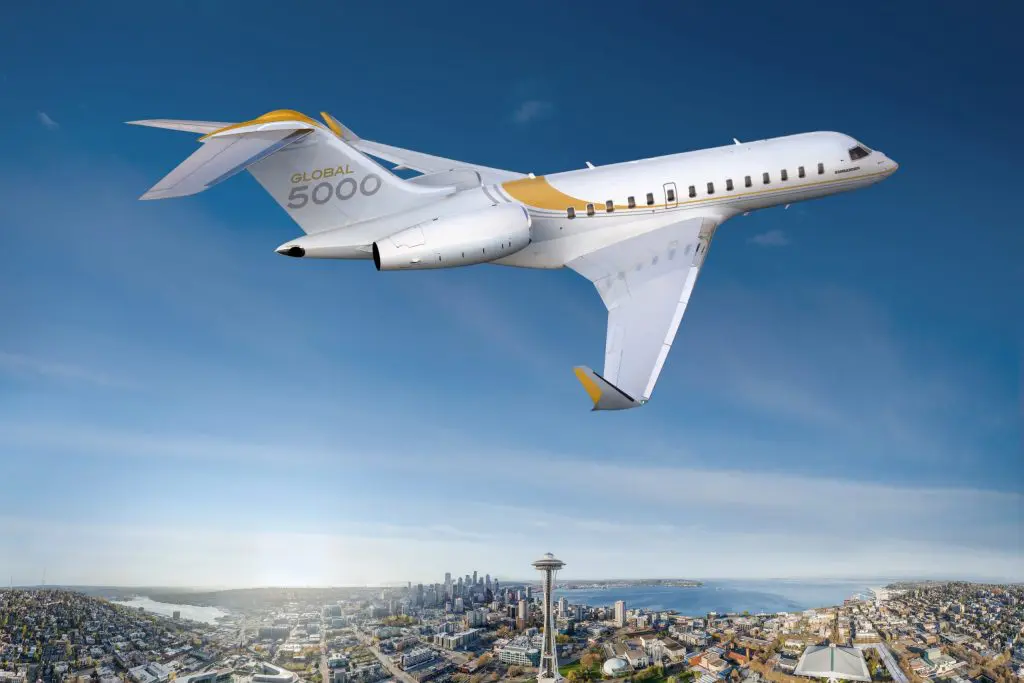 A private jet flying over a cityscape with clear skies.