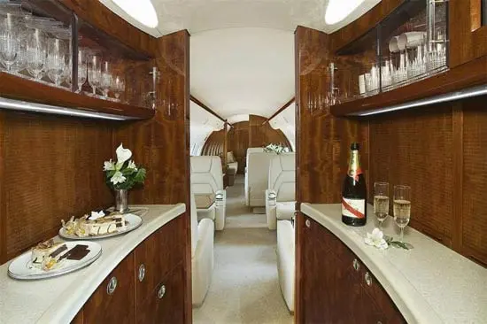 Luxurious interior of a private jet with wooden cabinetry and plush seating.