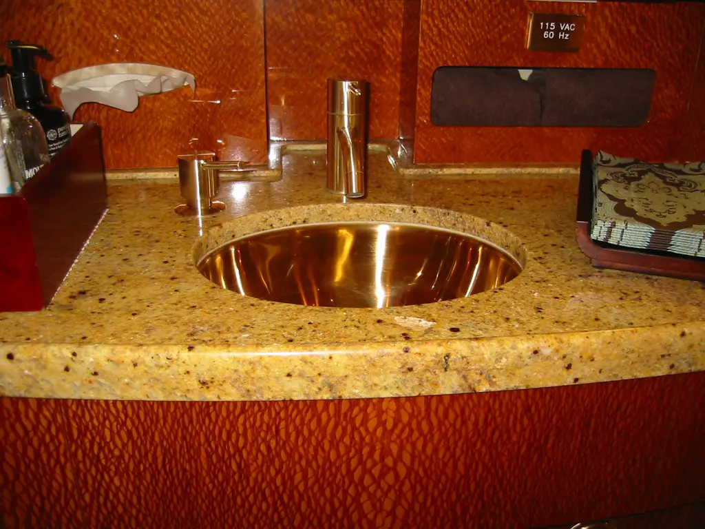 A modern bathroom sink with a polished brass basin and granite countertop.