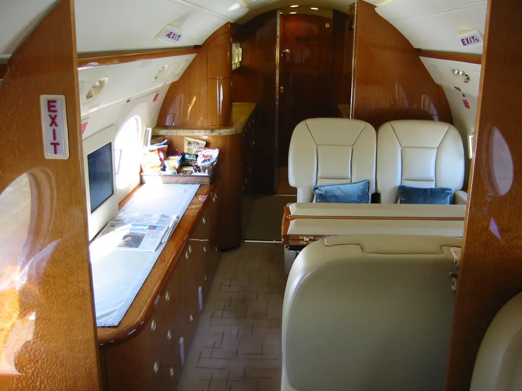 Interior of a private jet with leather seats and wooden cabinetry.