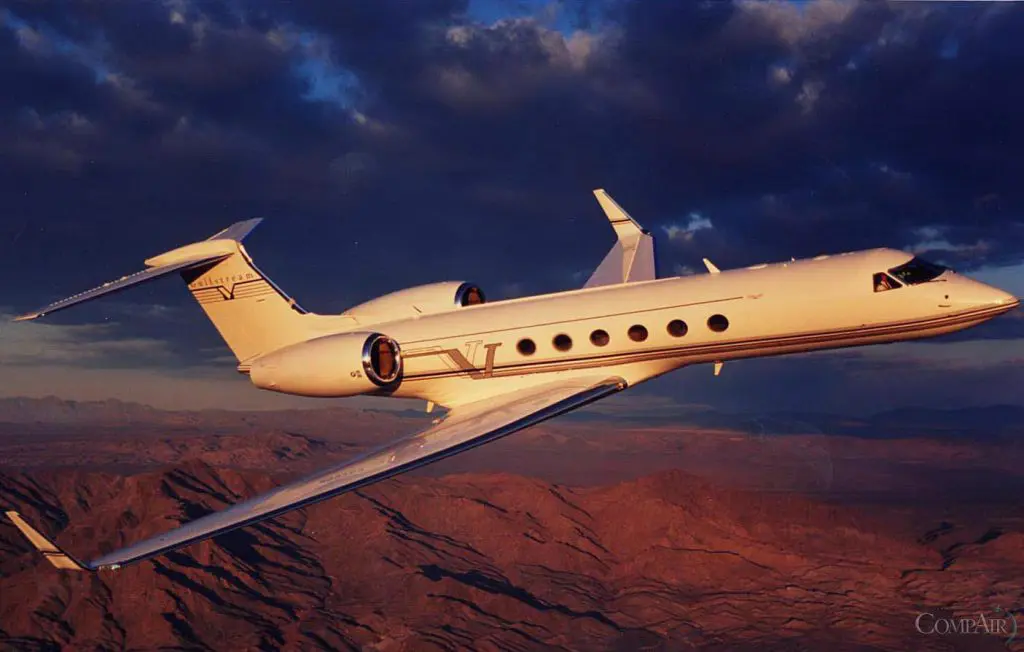 A sleek private jet flying over a rugged desert landscape at sunset.