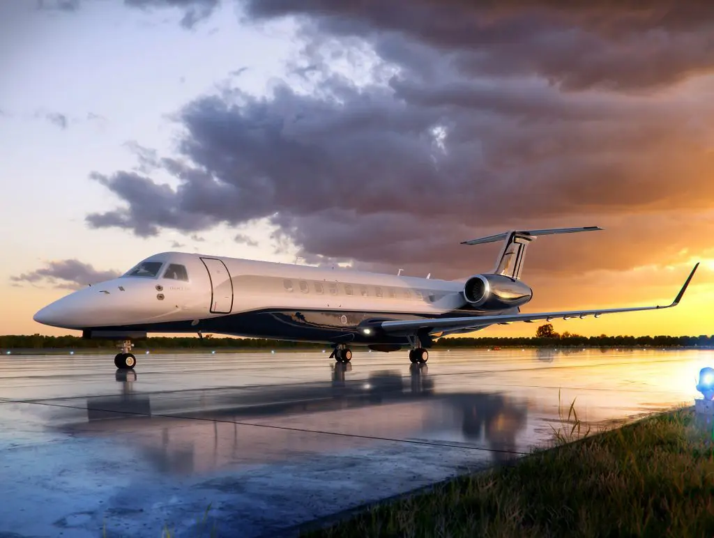 A sleek private jet parked on a wet runway at sunset.