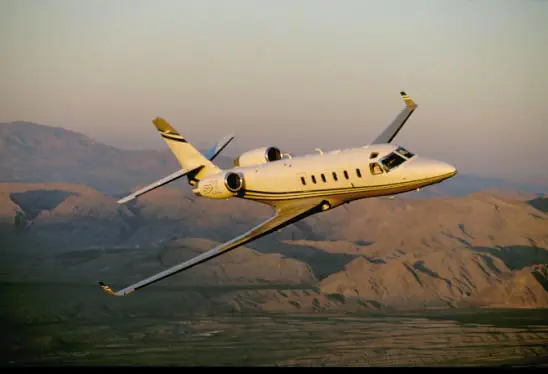 A private jet flying over mountainous terrain during sunset.