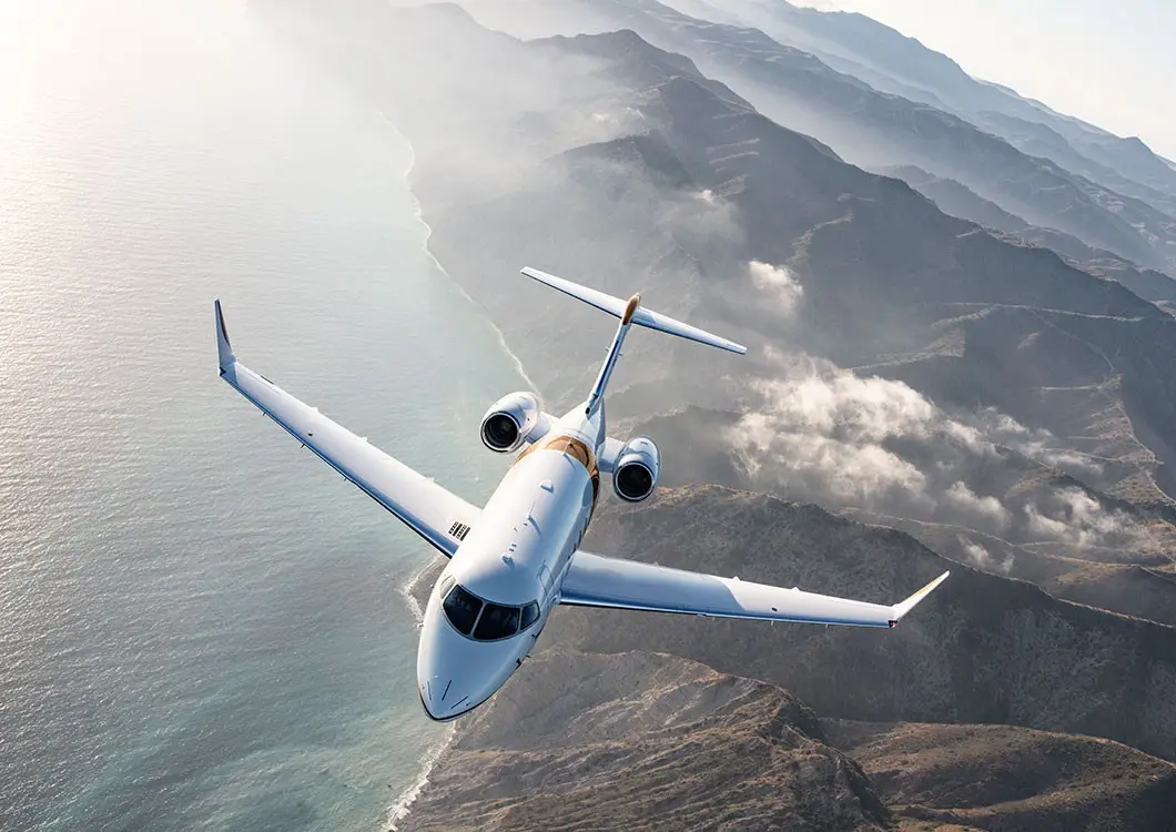 A private jet flying over mountainous terrain through clouds.