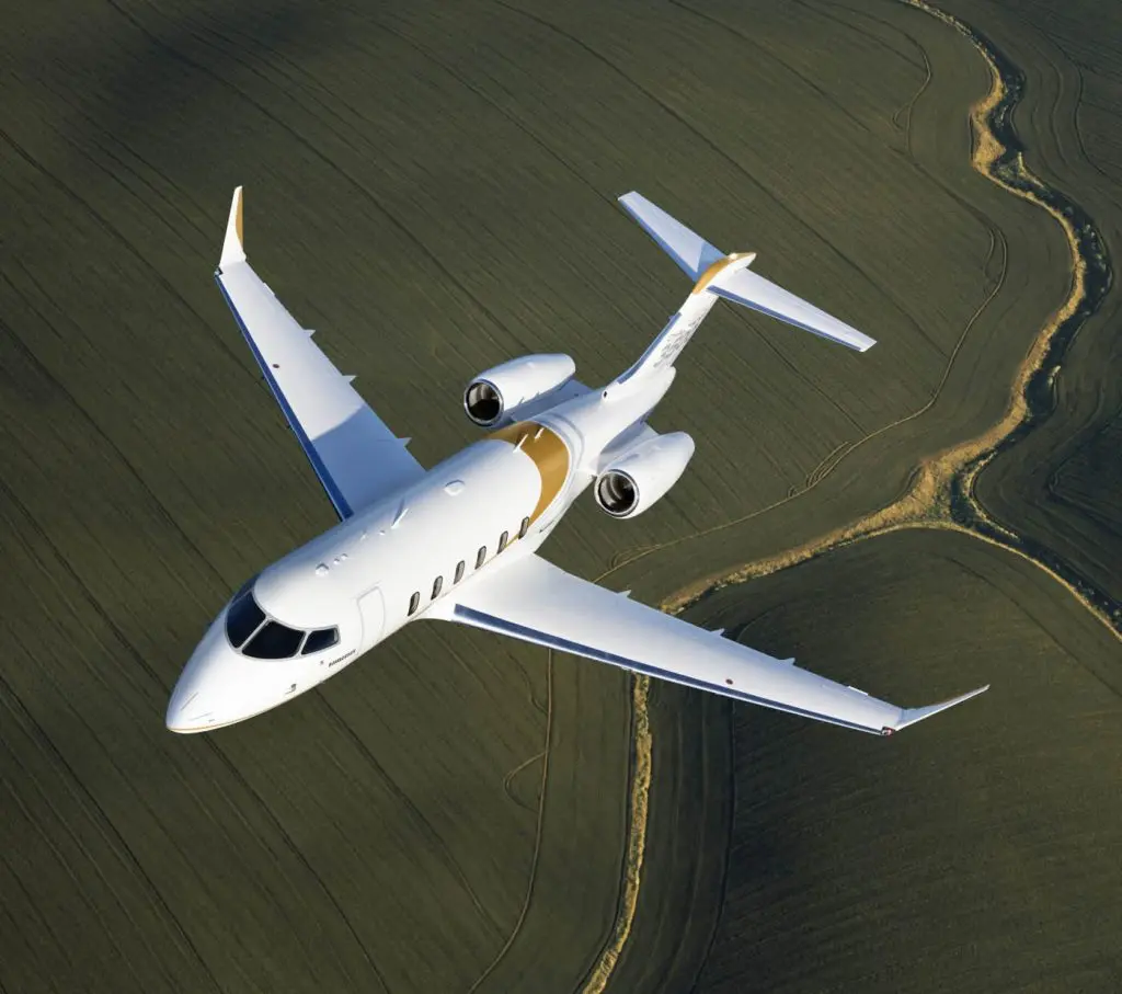 A white private jet flying over green fields.