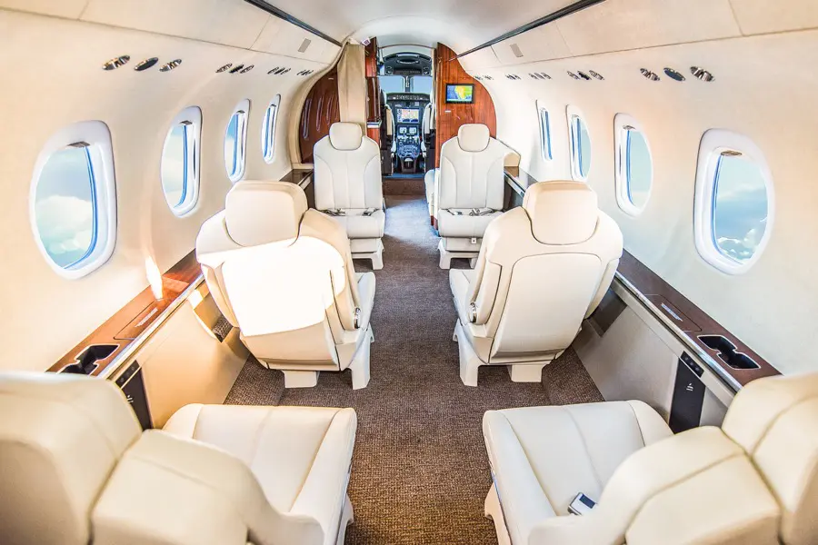Luxurious private jet interior with cream leather seats and wood accents.
