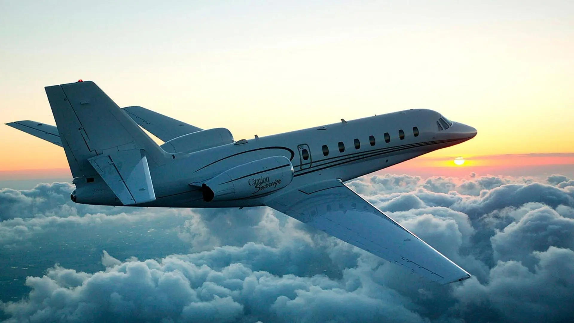 A private jet flying above the clouds during sunset.