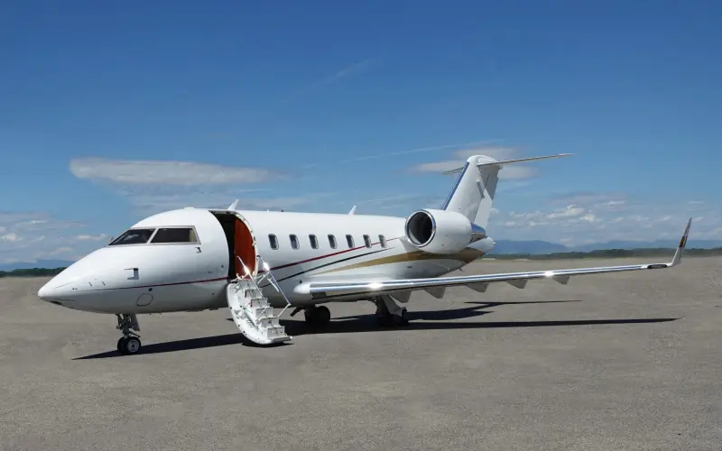 Private jet parked on tarmac with open door and stairs.