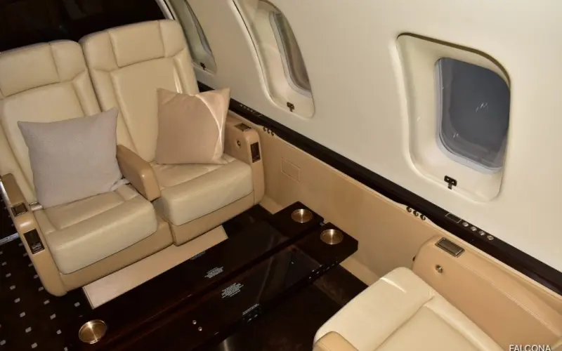 Luxurious private jet interior with cream leather seats and polished wood table.
