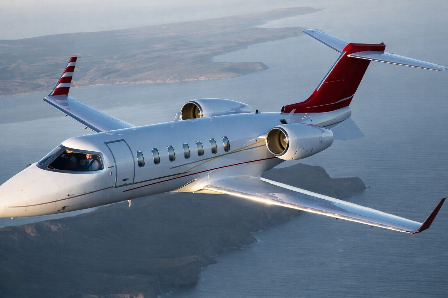 A sleek private jet flying over a coastal area.