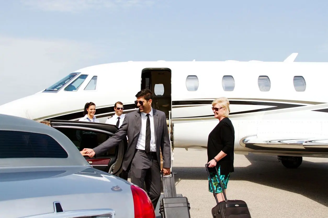 Businessman with luggage near a private jet and luxury car.