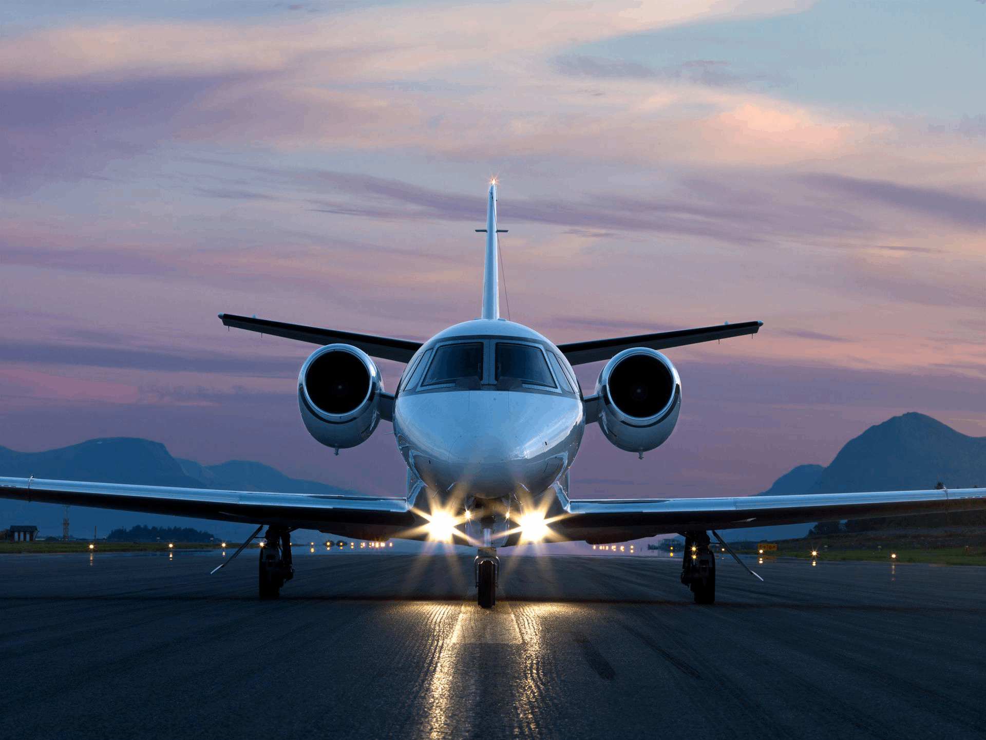 A private jet on runway at dusk with lights on.