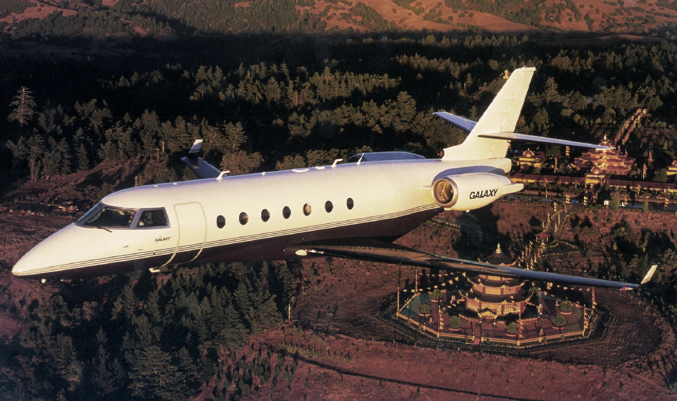 A private jet flying low over a desert landscape at sunset.