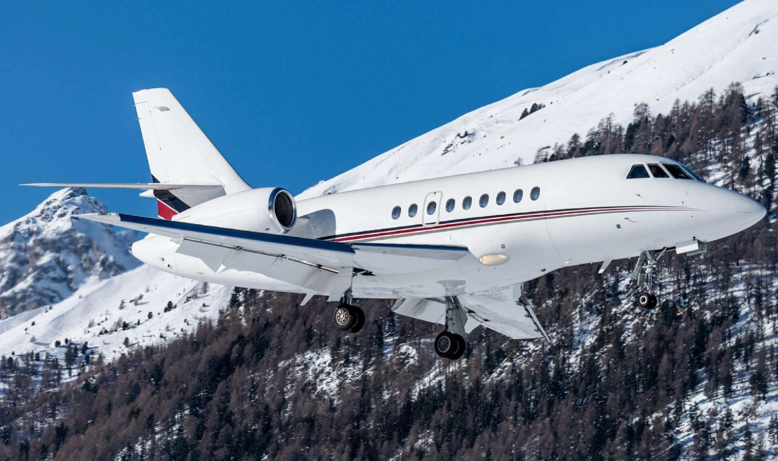 Private jet flying over snowy mountain landscape under clear blue sky.
