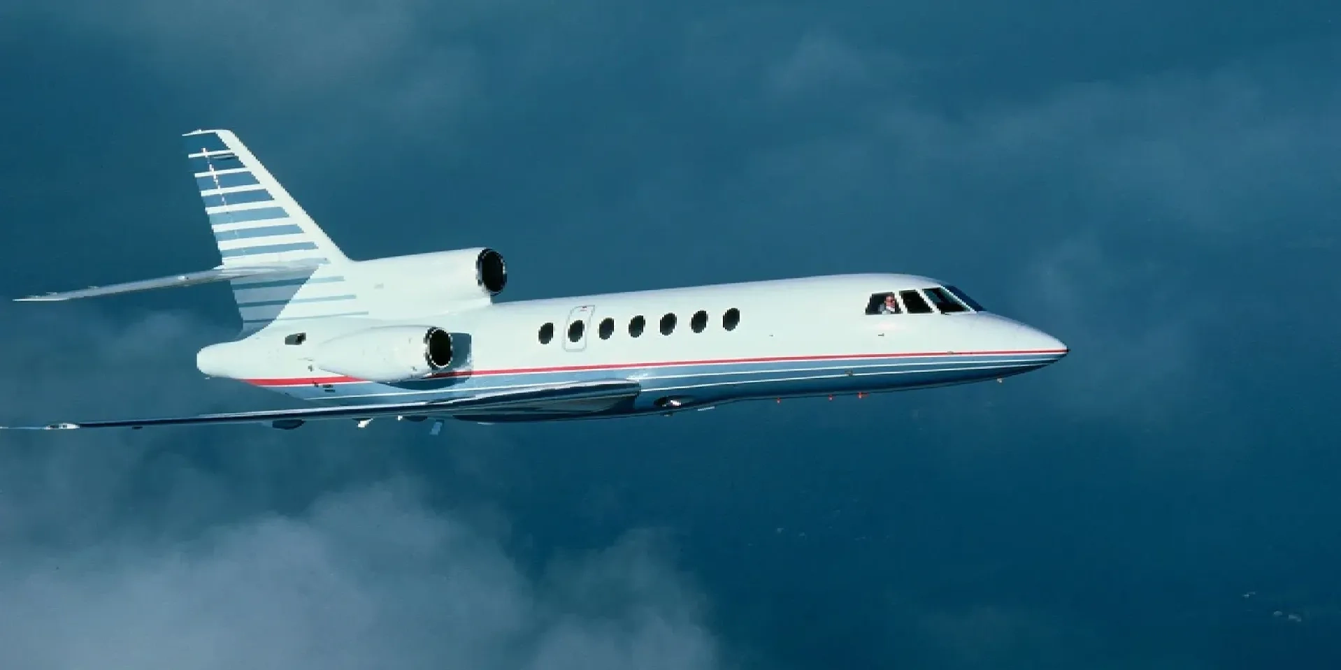A sleek private jet flying against a cloudy blue sky.